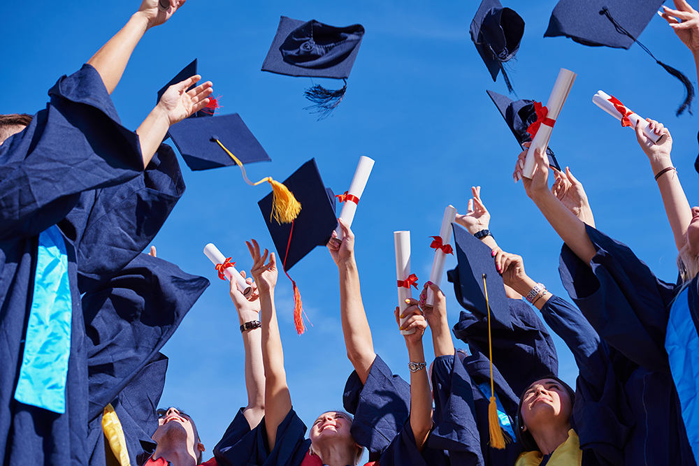 high school students graduates tossing up hats over blue sky.